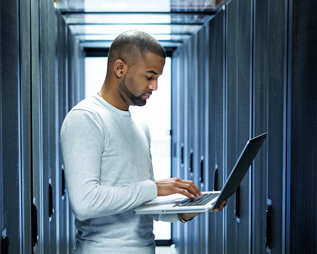 Workload Migration &ndash; A male IT technician works on a laptop in a server room